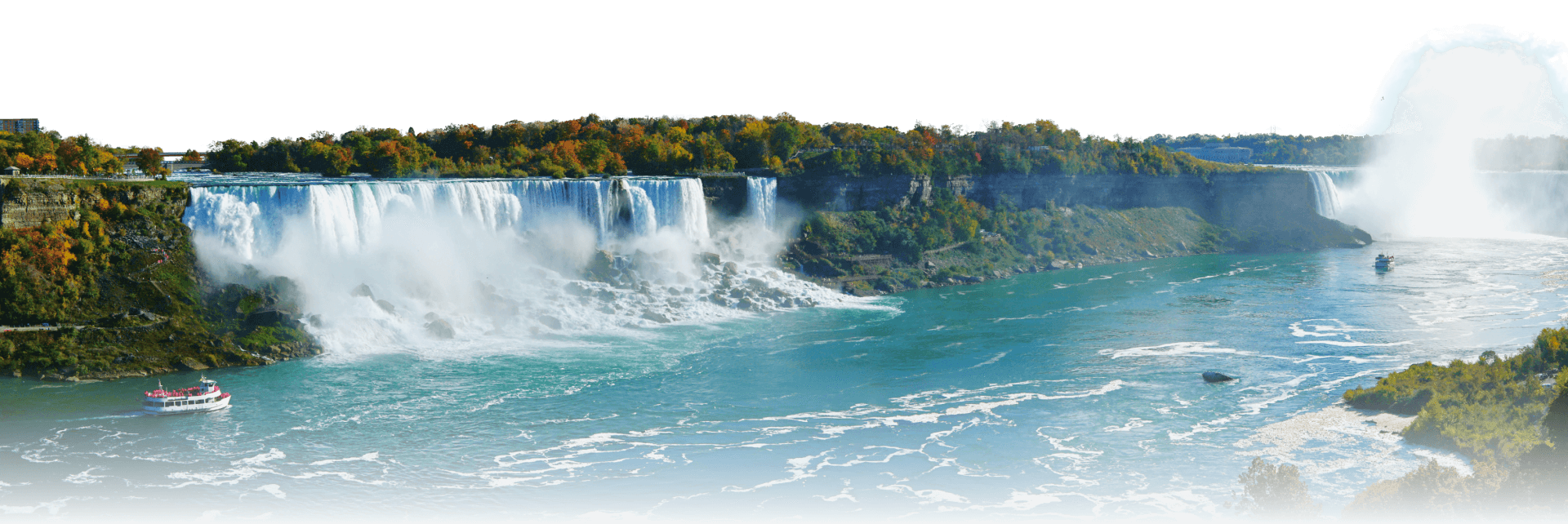 A panoramic view of Niagara Falls with mist rising from the cascading water, colorful autumn trees in the background, and two tour boats on the river below