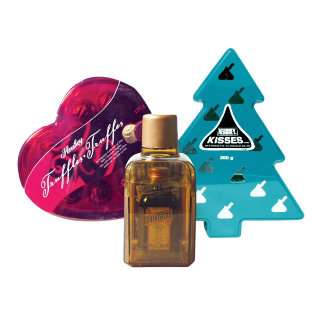 A festive assortment featuring a heart-shaped box of Hershey’s Truffle chocolates, a teal Christmas tree-shaped Hershey’s Kisses gift box, and a small amber bottle of Cointreau liqueur
