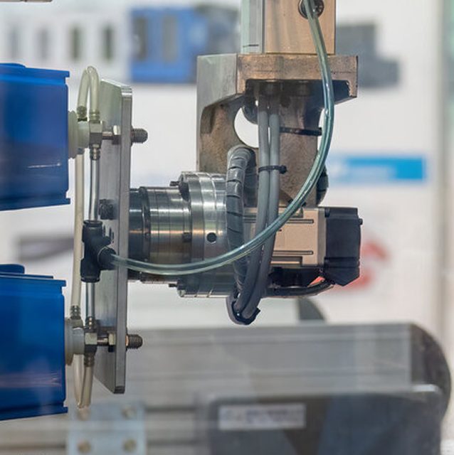 Close-up of a robotic arm or industrial machine part with wiring and blue plastic components, likely used in automated manufacturing or assembly