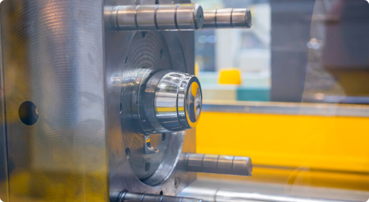 Close-up view of a precision metal mold inside an injection molding machine, with multiple cylindrical guide pins and a highly polished central cavity, set in a manufacturing environment
