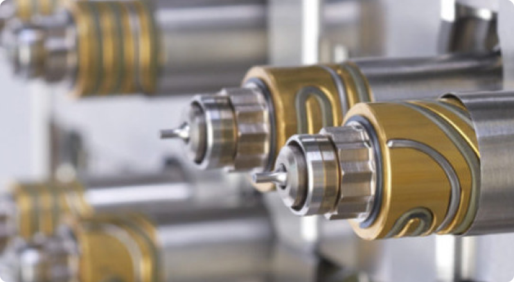 Close-up view of precision-engineered industrial nozzles or injection molding components, featuring gold and silver metallic finishes arranged in a symmetrical, high-performance manufacturing setup