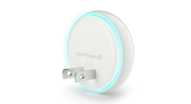 A white circular smart device from Hunter Douglas with a glowing blue ring light, designed to plug into a wall outlet using two metal prongs