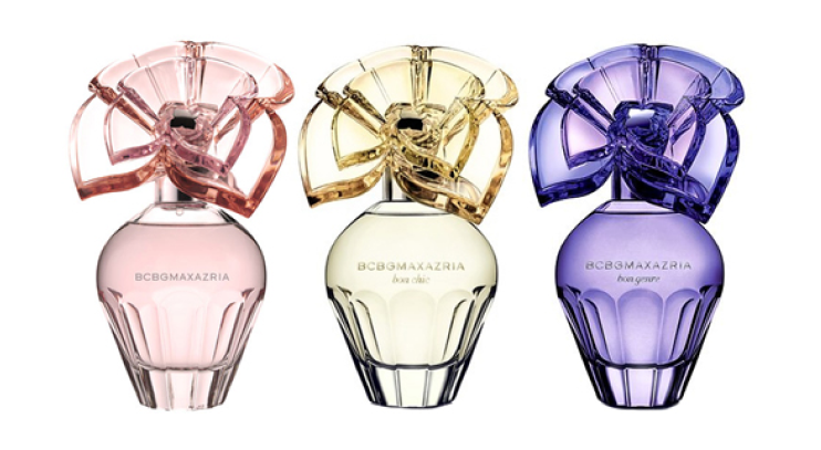 Three BCBGMAXAZRIA perfume bottles in soft pink, pale yellow, and lavender, each with a sculpted flower-like cap and elegant curved glass design