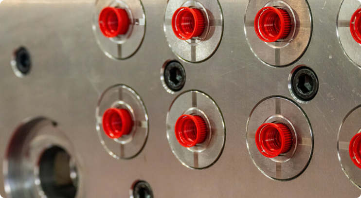Close-up of a precision injection mold tool with multiple red plastic components formed in circular cavities on a metallic mold plate