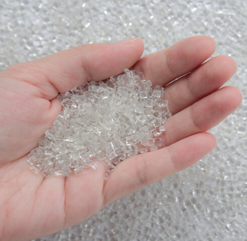A hand holding a pile of clear plastic resin pellets used as raw material in plastic manufacturing