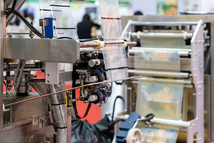 Close-up of automated packaging machinery feeding clear plastic film through rollers for food product wrapping in a factory setting