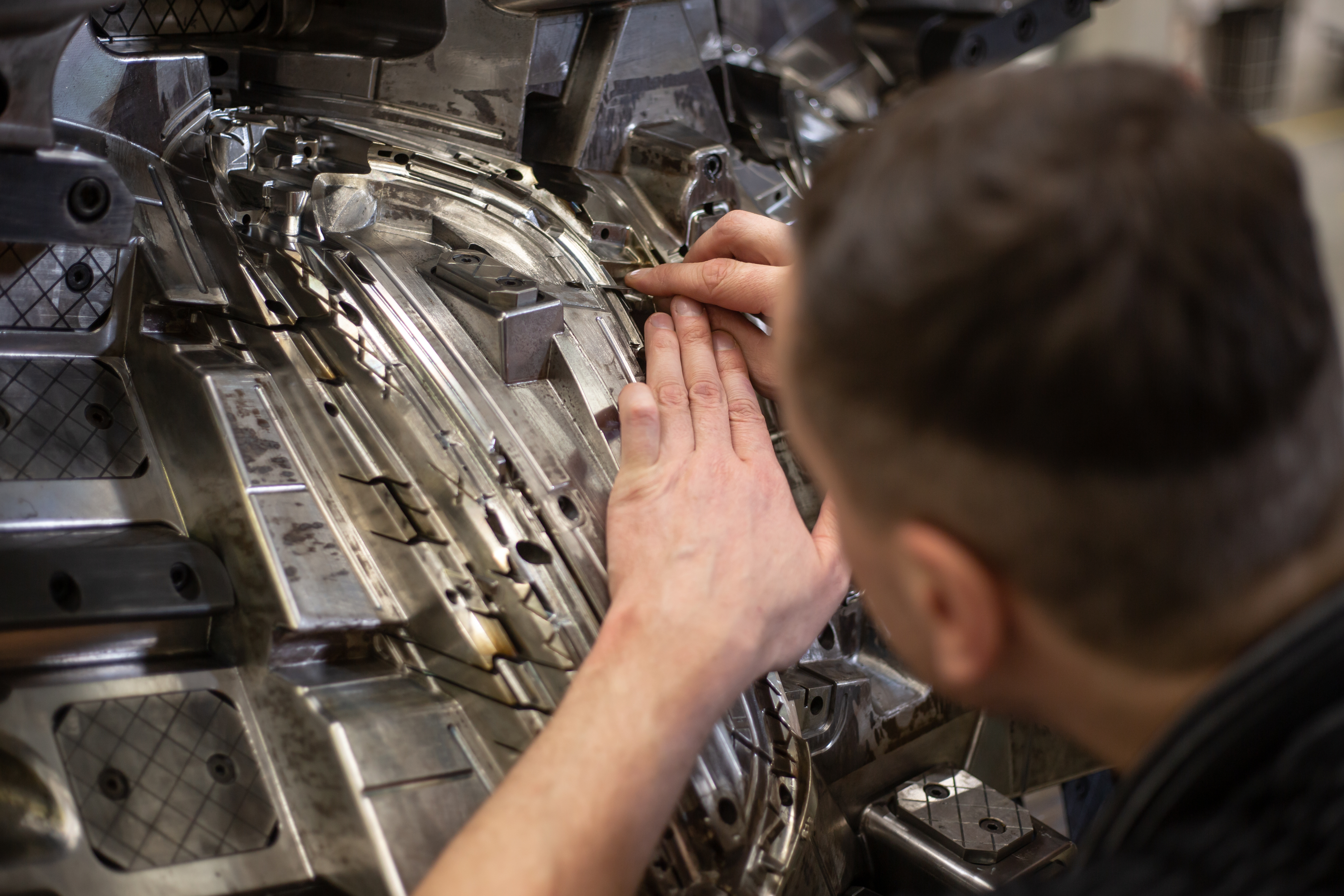 A technician closely inspects and adjusts a large, complex metal mold used in industrial manufacturing